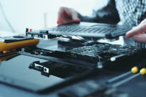 Technician repairing and refurbishing a laptop with the top cover removed, showcasing internal components. Refurbished Product.